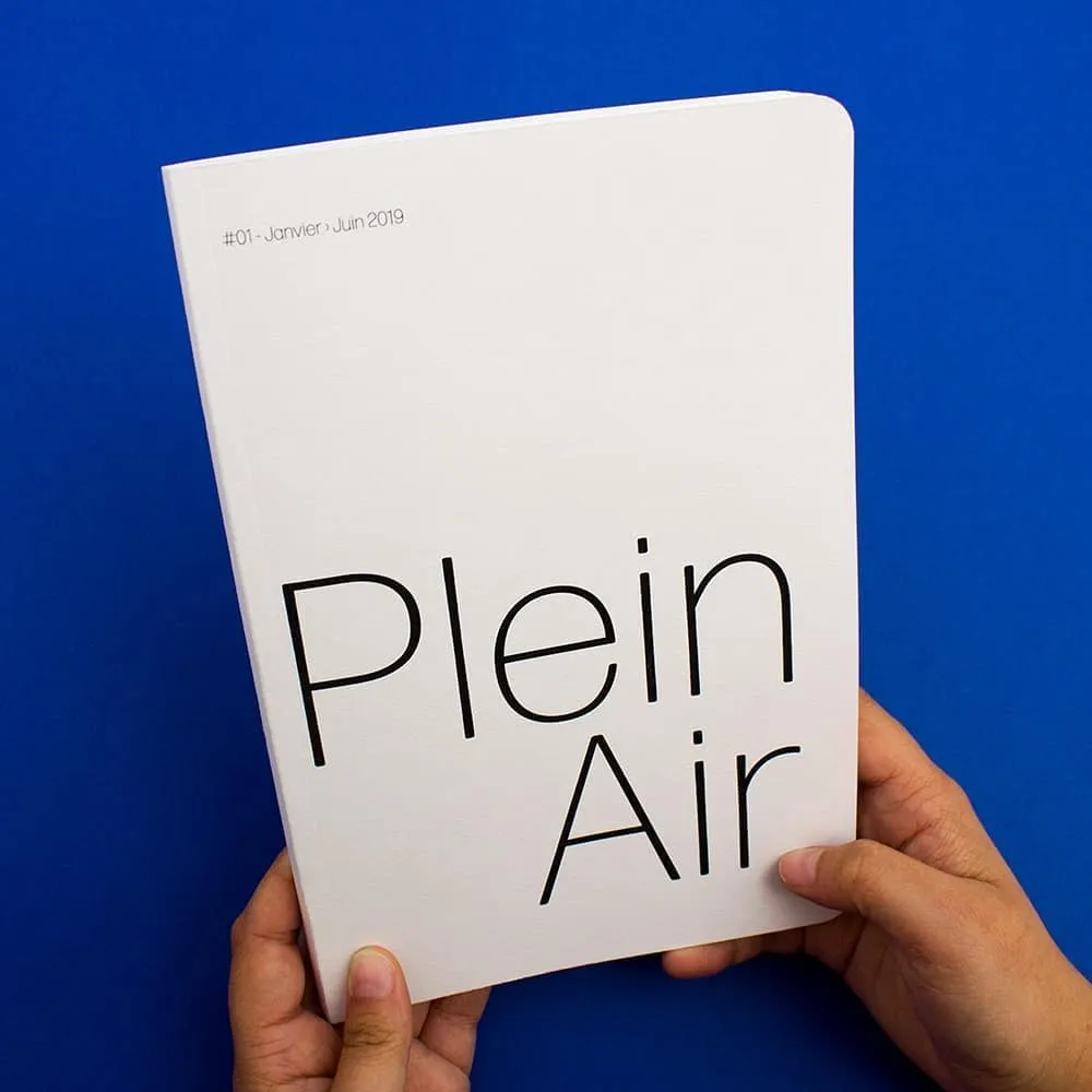 Livre tenu fermé, de face, la couverture est blanche avec les mots "Plein Air" écrit en grand et finement.